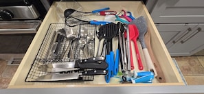 Un tiroir de cuisine contenant divers ustensiles et ustensiles de cuisine, notamment un fouet, une spatule et un grand couteau.