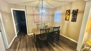 A dining area with a wooden table and chairs, a chandelier, and artwork on the walls.
