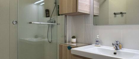 A modern bathroom with a glass shower enclosure, a wooden vanity, and a mirror above the sink.