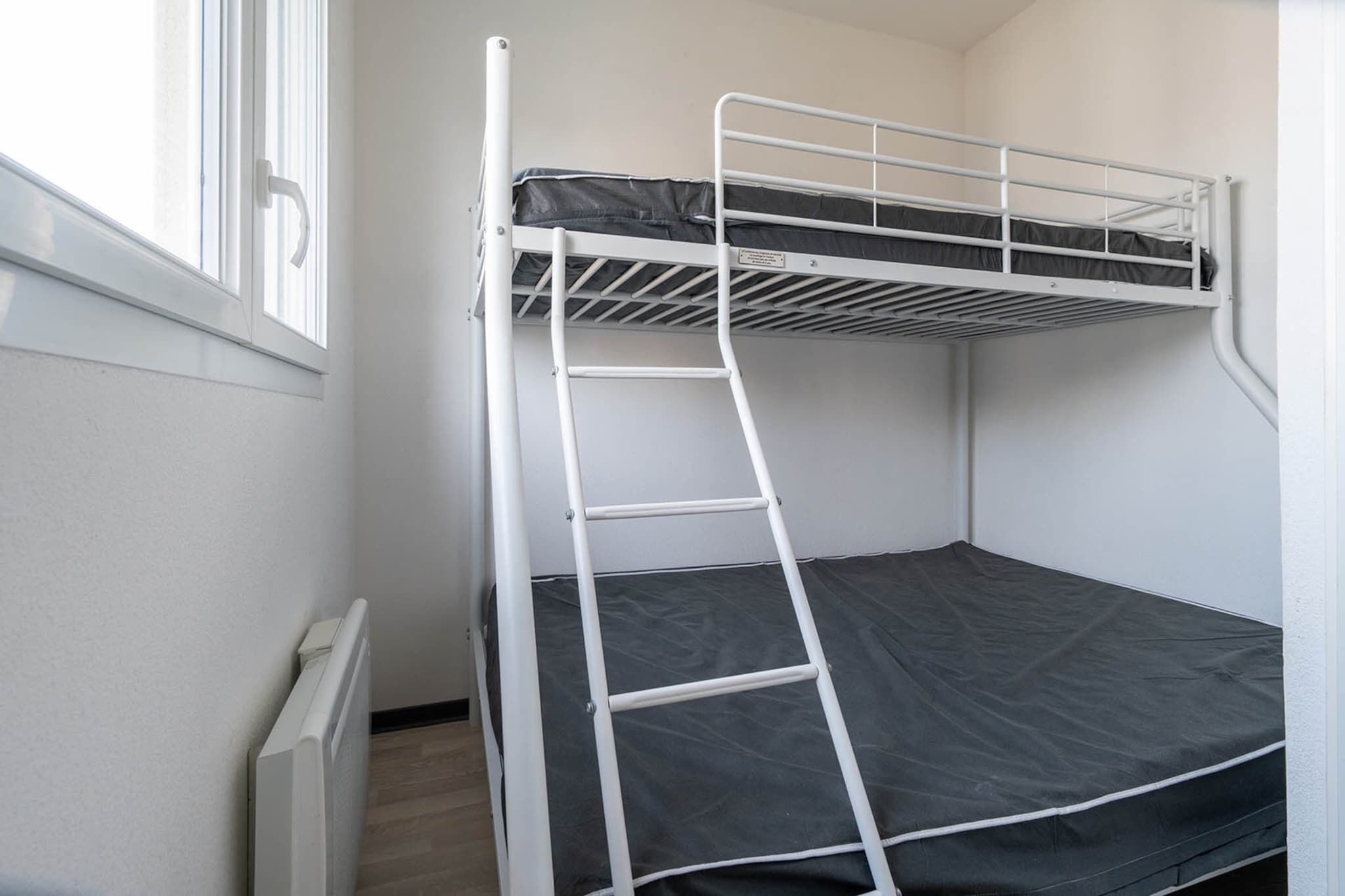 Ein Etagenbett mit einer Leiter, einem Fenster und einer Heizung.