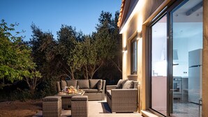 An outdoor patio with wicker furniture, a dining table, and a view of the kitchen through a glass door. - Seaside Villa Angel - Samos Cozy Getaway (Samos)