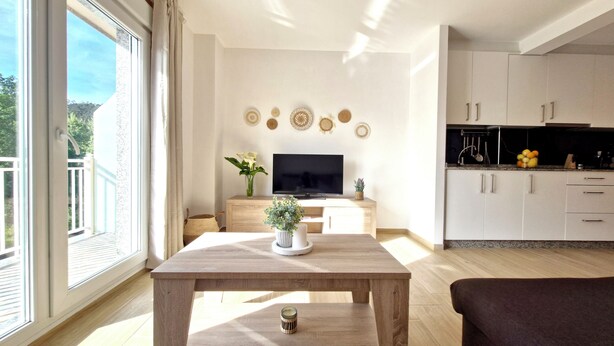 A modern living room with a wooden table, a TV, and a kitchen area with white cabinets. - APARTMENT WITH TERRACE FOR 4 PEOPLE (Mondariz)