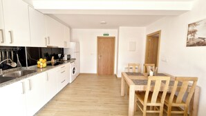 A modern kitchen with white cabinets, a granite countertop, and a built-in washing machine. There is a dining area with wooden chairs and a table. - APARTMENT WITH TERRACE FOR 4 PEOPLE (Mondariz)