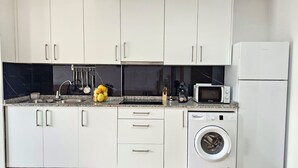 A modern kitchen with white cabinets, a granite countertop, a microwave, a washing machine, and various kitchen utensils. - APARTMENT WITH TERRACE FOR 4 PEOPLE (Mondariz)