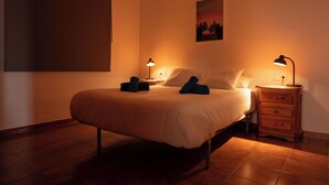 Ein ordentlich bezogenes Bett mit zwei Kissen und zwei gefalteten Handtüchern, ein Nachttisch mit einer Lampe sowie ein Wandbild.