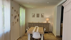 A dining area with a wooden table and chairs, a kitchen in the background, and a stone-tiled floor. - Country House (Caumont-sur-Durance)