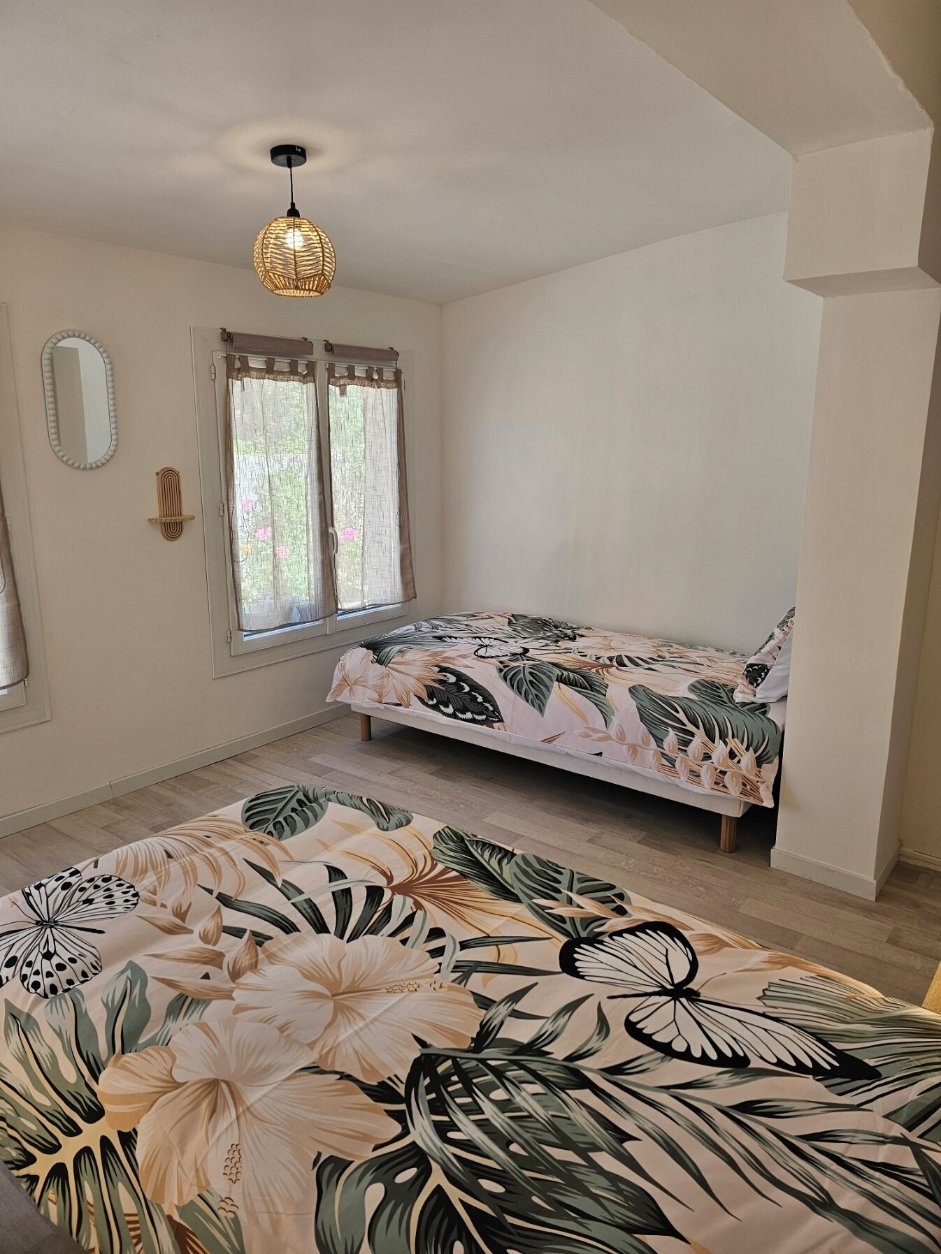 Une chambre à coucher avec un lit, une fenêtre avec des rideaux, un luminaire suspendu et un miroir au mur.
