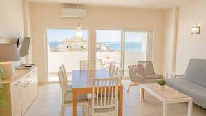 Un salon moderne comprenant un coin repas, un canapé, une table basse et un téléviseur. Il y a également un balcon avec vue sur la mer.