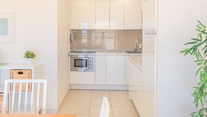 Une cuisine moderne avec des meubles blancs, un four à micro-ondes et un évier. On y trouve une table à manger avec des chaises et une plante en pot.