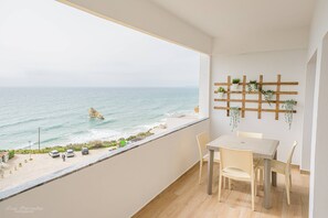 Ein Balkon mit Blick auf den Ozean, einem Tisch mit Stühlen und einem Holzregal mit Pflanzen.