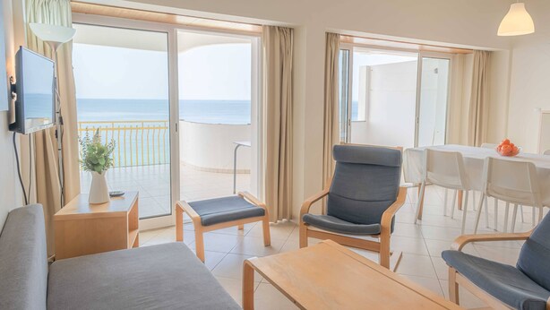 Quarto de hotel com varanda, televisão, área de refeições e sofá.