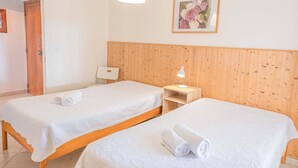 Quarto de hotel com duas camas de solteiro, cabeceira de madeira, mesa de cabeceira com abajur e quadro na parede.