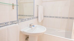 Casa de banho com lavatório branco, prateleira de vidro, banheira e espelho.