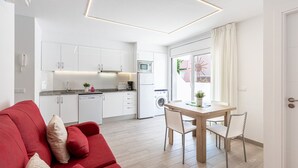 Une cuisine moderne avec des meubles blancs, un coin repas doté d’une table et de chaises en bois, et un canapé rouge.