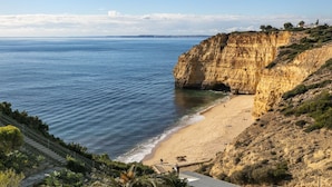 A coastal cliff with a beach, a staircase leading down to the beach, and a clear view of the sea.