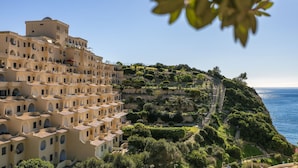 A coastal hotel with multiple balconies, a staircase leading to the top, and a view of the sea.