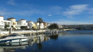 Una propiedad frente al agua con un puerto deportivo, edificios blancos con techos de tejas rojas y palmeras.