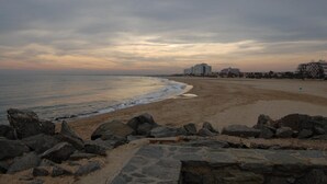 Una playa con primer plano rocoso y una hilera de edificios al fondo.