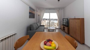 Una sala moderna con una mesa de comedor, un sofá, un ventilador de techo y vistas amplias a través de grandes ventanales.