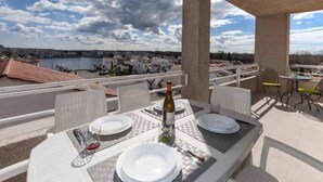 Un espacio exterior para comer con una mesa dispuesta para dos, con vistas a un cuerpo de agua y un pueblo.