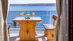 A wooden table with two glasses of orange juice and a plate of food, set against a scenic ocean view.