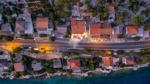 An aerial view of a coastal residential area with houses, a road, and a body of water.