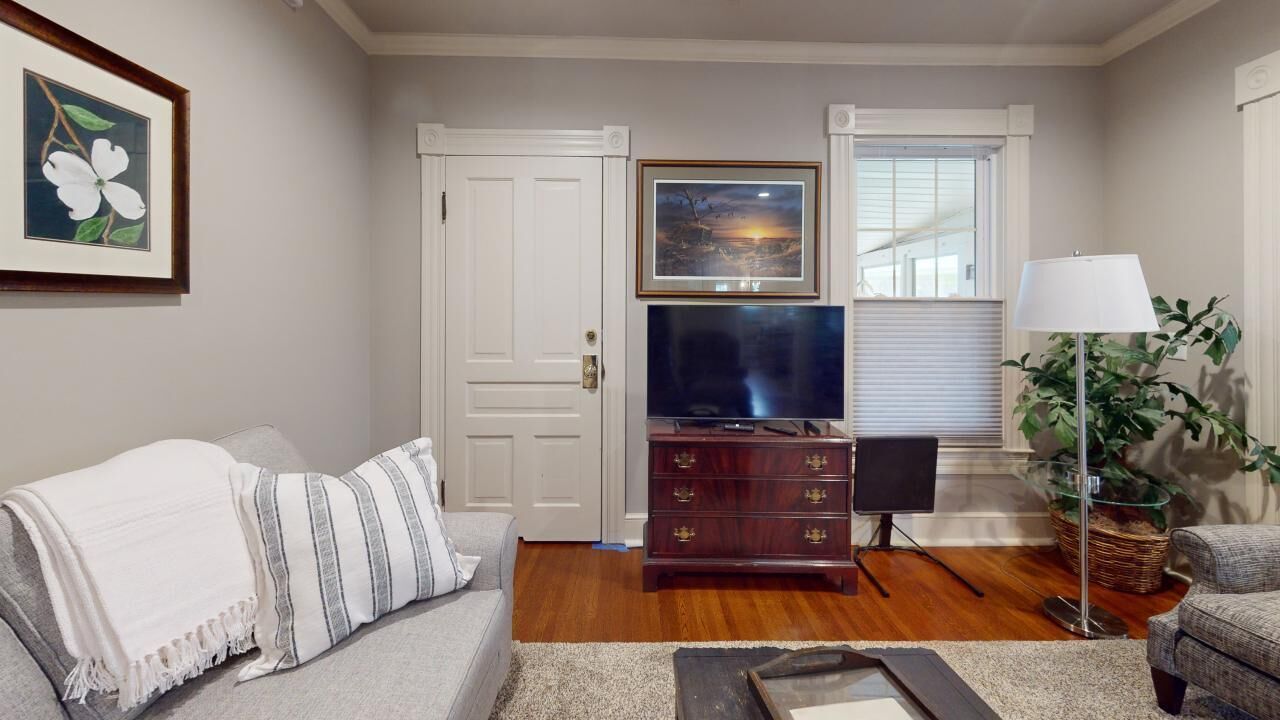 A living room with a grey sofa, a striped throw blanket, a wooden cabinet with a flat-screen TV, a standing lamp, and a framed picture on the wall.