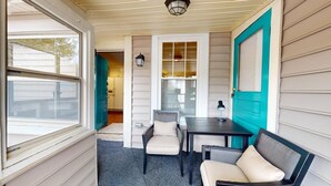 Een veranda met een tafel, twee stoelen, een raam en een deur met blauwgroene details.