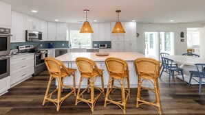 Una cocina moderna con armarios blancos, una isla grande con taburetes y una zona de comedor con sillas azules.