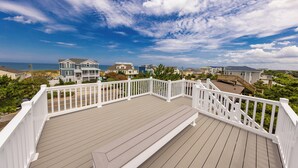 Una terraza de madera con barandillas blancas que da vista a una zona residencial con casas y un cielo despejado.