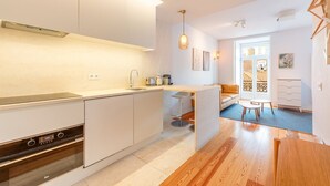 A modern kitchen with white cabinetry, a built-in oven, and a dining area with a wooden table and chairs. - GuestReady - Downtown Charming Stay (Lisbon)