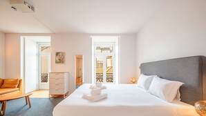 A hotel room with a large bed, a wooden desk, a chair, and a view of a balcony with a railing. - GuestReady - Downtown Charming Stay (Lisbon)