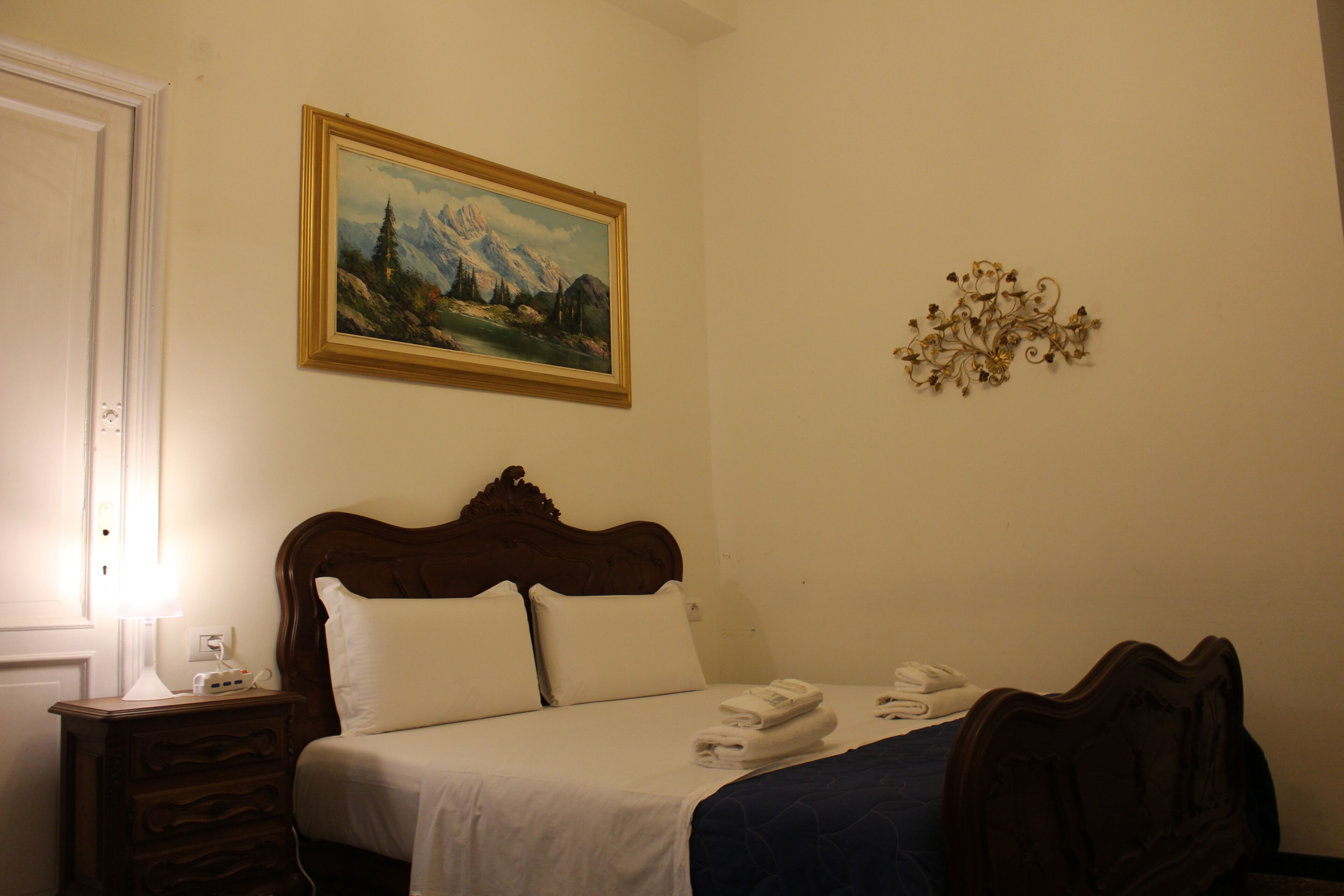 A hotel room with a bed, a nightstand, a lamp, a painting, and a wall decoration.