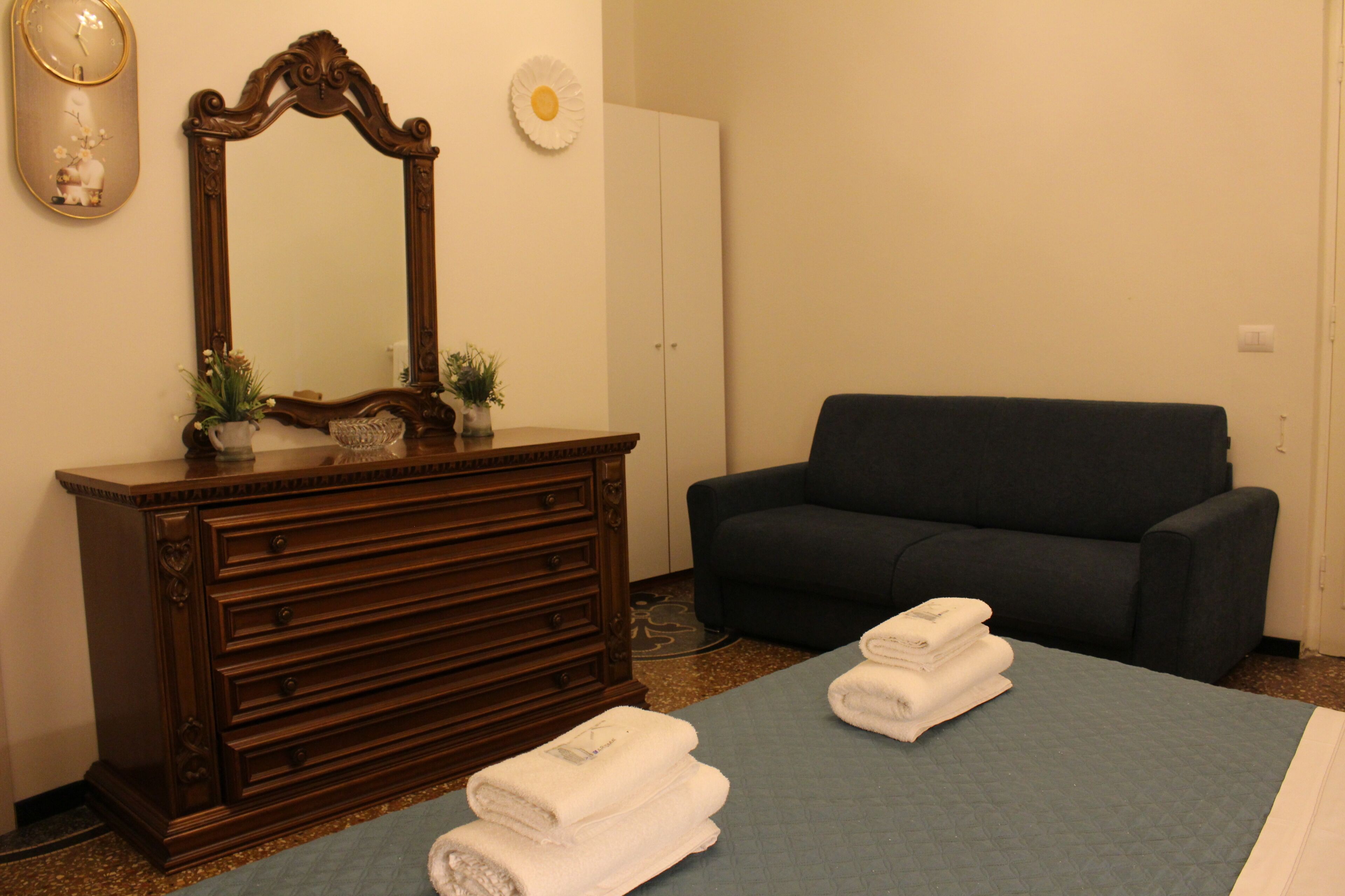 Una habitación con un aparador de madera, un espejo, un sofá oscuro y dos toallas sobre un felpudo azul.