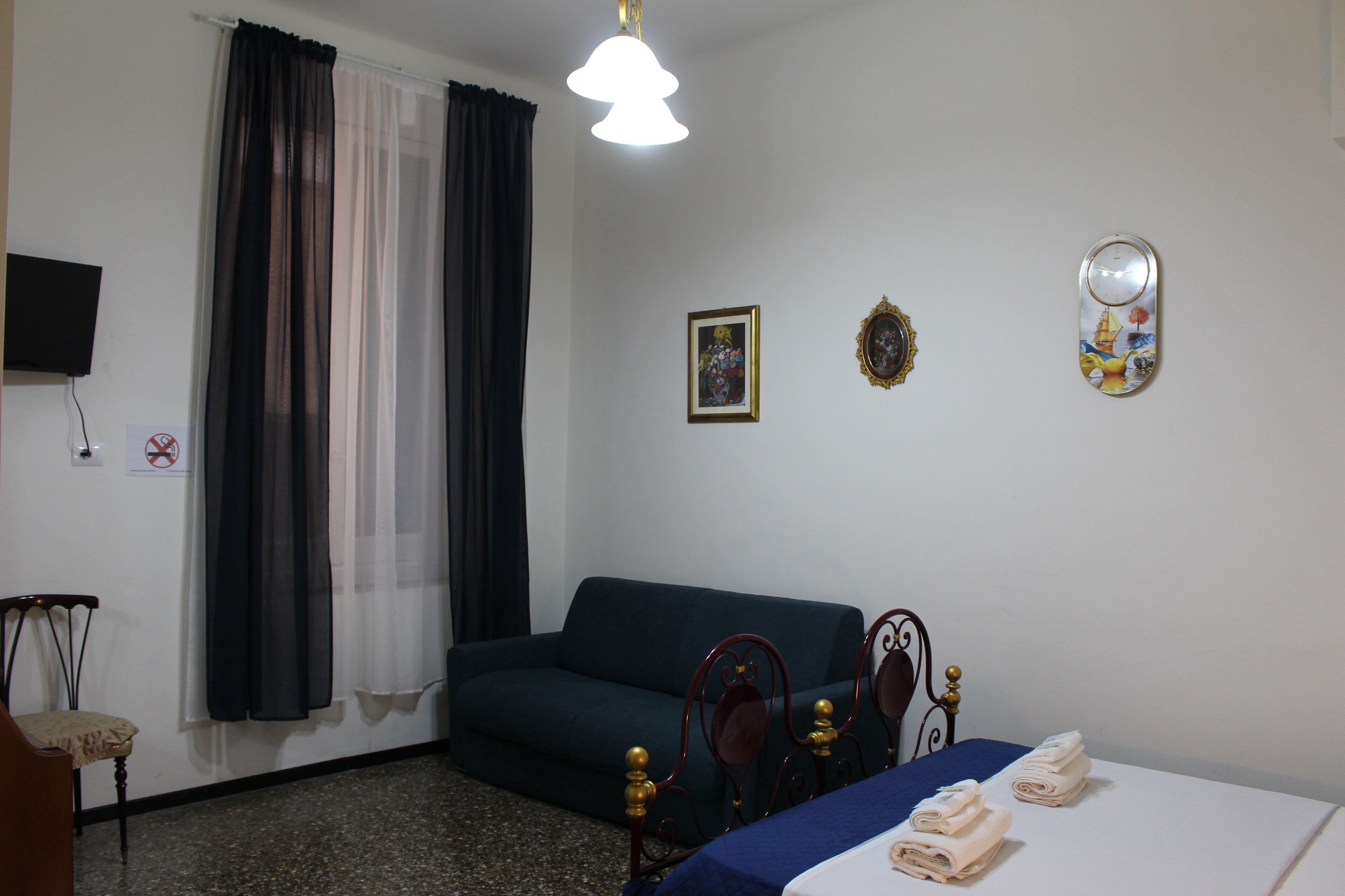 A hotel room with a bed, a sofa, a chair, a television, and a window with curtains.