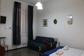 Habitación de hotel con cama, sofá, sillón, televisor y ventana con cortinas.