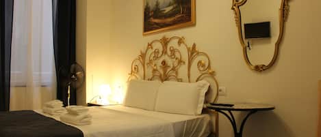 Habitación de hotel con cama, mesita de noche, escritorio, silla, ventilador, un cuadro y un espejo.