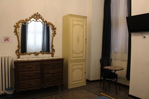 A room with a wooden dresser, a tall cabinet, a small round table, and a radiator. - Genova Antica (Genoa)