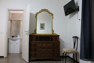 Een kamer met een houten dressoir, een spiegel, een klein geborduurd plaatje, een aan de muur bevestigde televisie en een deur naar een badkamer.