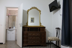 Una habitación con un aparador de madera, un espejo, un pequeño cuadro enmarco, un televisor montado en la pared y una puerta que da a un baño.