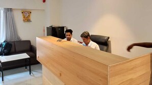 Un bureau moderne avec un comptoir d’accueil en bois, un canapé noir et un rideau gris.