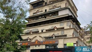 Un immeuble à plusieurs étages abrite un hôtel appelé « Legacy Inn » au rez-de-chaussée. Plusieurs voitures sont garées devant, et l’immeuble possède de nombreux balcons.