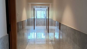 Un couloir doté d’un plancher ciré, une porte en bois sur la gauche et une grande fenêtre au fond.