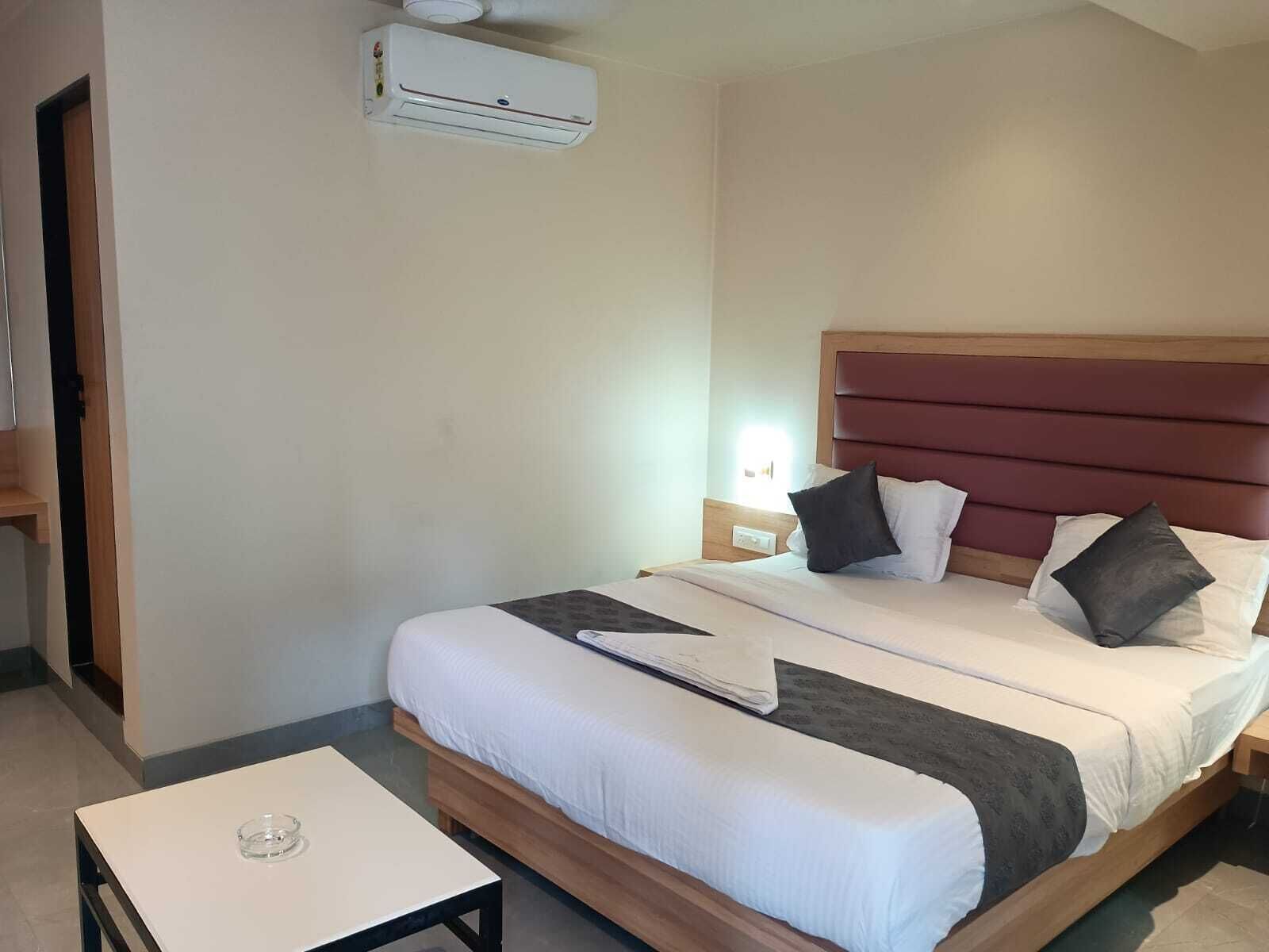 Una habitación de hotel con cama, mesitas de noche, un aire acondicionado y una pequeña mesa.