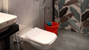 Une salle de bain moderne avec un mur en marbre, un lavabo blanc, une douche équipée d’un pommeau de douche à main et un seau rouge.