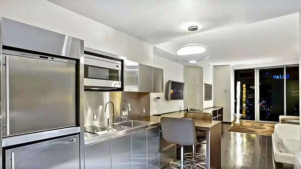 A modern kitchen with stainless steel appliances, a bar area, and a view of the city at night.