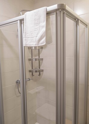 A glass-enclosed shower stall with a white towel hanging on the door, a chrome shower head, and a small shelf. - Lovely view Apartment (Portimão)