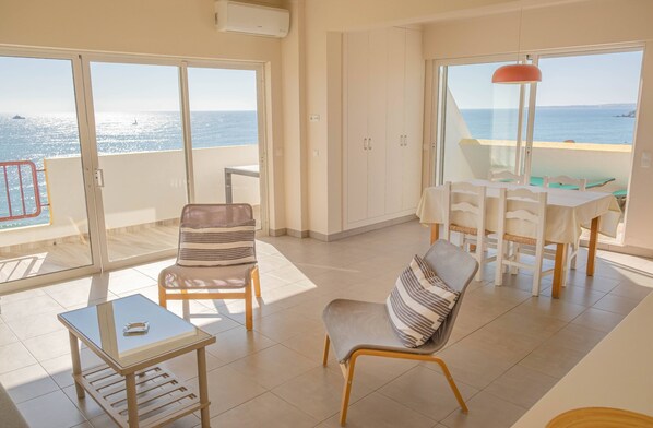 A spacious balcony with a view of the sea, a dining area with white chairs, and a table with a glass top. - Lovely view Apartment (Portimão)