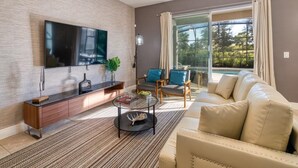 A modern living room with a flat-screen TV, a sofa, a coffee table, and a large window with curtains. - Solterra 6BR | Private Pool & 4 Ensuites (davenport)