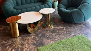 A modern lounge area with a wooden wall, a ceiling fan, a potted plant, and two green upholstered chairs. - Pink Guava  (Gurugram)